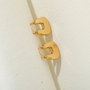 Macro view of geometric U-shaped earrings in polished 14K gold finish with creative shadows