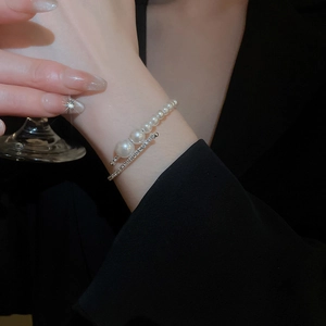 Detail of layered pearl bracelet with crystals on model holding a crystal glass
