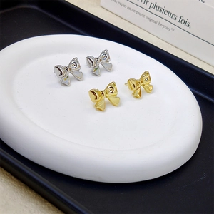 Elegant bow knot stud earrings in gold and silver finish on a ceramic tray