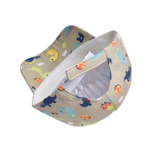 Detail of baby beige baseball cap featuring cartoon dinosaur prints and adjustable strap