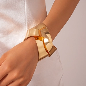 Close-up of a wide polished gold knot cuff bracelet with layered metallic texture