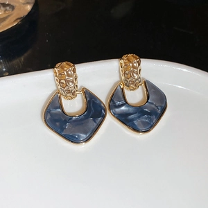 Macro view of blue marble acrylic pendant earrings with textured gold metal detail