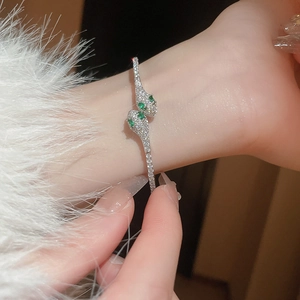 Detailed close-up of a silver snake-shaped cuff bracelet with emerald eyes and zircon stones