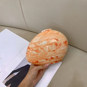 Detailed view of an oval evening clutch with orange marble pattern texture and glossy finish