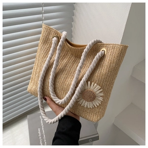 Detail of woven straw tote bag featuring white daisy flower and thick rope handles