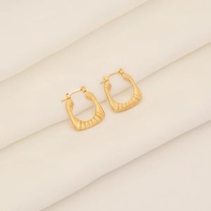 Macro shot of gold geometric square earrings with vintage striped texture on white fabric