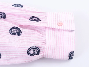 Gros plan du poignet d'une chemise à rayures roses avec broderie paisley et bouton