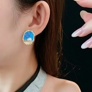 Dettaglio di orecchino vintage dorato con farfalla blu e perla su una modella