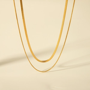Detail of a double-layered gold snake chain necklace with flat blade links on beige background