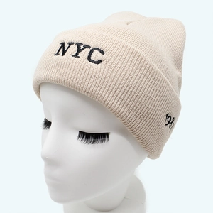 Close-up of knit beanie with NYC embroidery and 1983 side detail on beige fabric