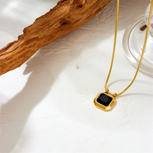 Close-up of a geometric black gemstone pendant on a gold snake chain necklace