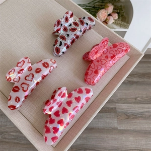 Medium plastic hair claws featuring red lips and heart patterns on a woven tray