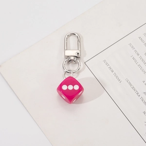 Detail of rose pink dice keychain with silver metal D-ring hook on a minimalist background