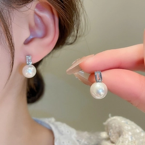 Close-up of a silver-tone earring featuring a round white pearl and a rectangular zircon