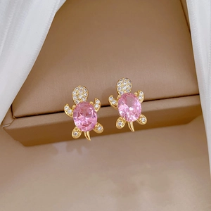 Detailed close-up of golden turtle stud earrings with pink gemstone and white zircon stones