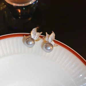 Macro shot of butterfly wing stud earrings with grey pearls on a white porcelain rim