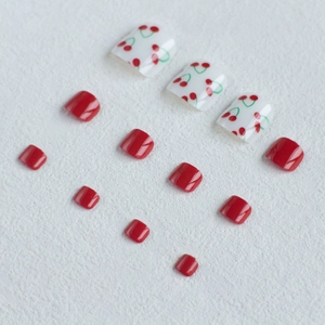 Detailed view of cherry pattern press-on toenails in red and white on textured fabric