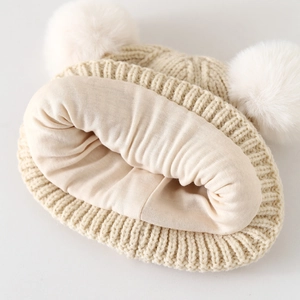 Detail der weichen beigen Strickstruktur und des warmen Innenfutters der Doppelbommelmütze