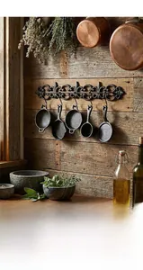 Dettaglio di un set da cucina decorativo in ghisa appeso su parete in legno scuro
