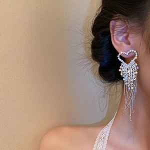 Side view of elegant heart-shaped tassel earrings with sparkling rhinestones on a model