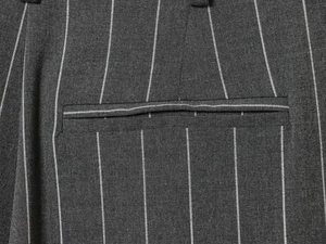 Détail du tissu gris à fines rayures et poche passepoilée soignée sur le pantalon