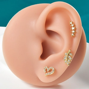 Close-up of gold stainless steel ear studs with leaf and heart shapes on a silicone ear