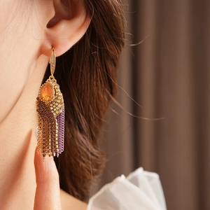 Close-up of bohemian layered gold tassel earrings with orange stones and purple beads