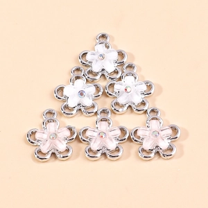 Enamel flower charms with rhinestones in white and pink, stacked on a warm beige background