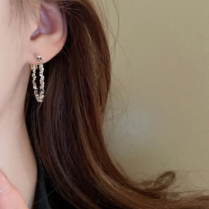 Close-up of a silver irregular textured hoop earring worn by a model in a side view