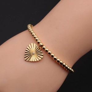 Close-up of a gold-plated heart pendant with sunburst texture on a beaded bracelet