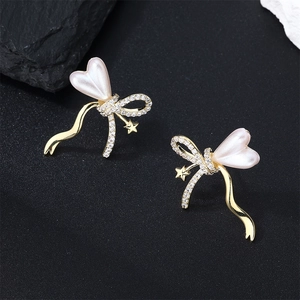 Elegant gold bow earrings with heart pearl and star charms on black rock background