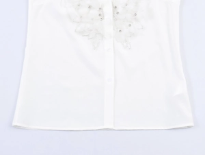 Détail d'un chemisier blanc sans manches avec dentelle, plumes et strass au col