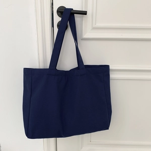 Detail of navy blue canvas tote bag hanging on a white door handle for daily use