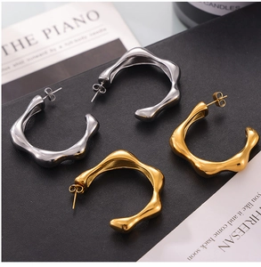 Detailed view of gold and silver irregular wave-shaped C-style earrings on textured base
