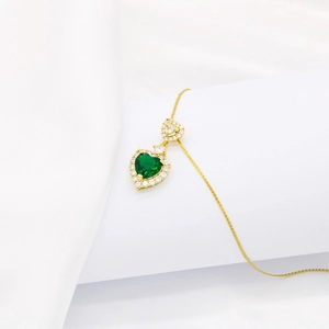 Close-up of gold heart necklace with emerald green gemstone and zircon settings