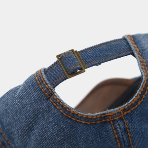 Detailed close-up of dark blue denim beret featuring orange stitching and copper metal buckle
