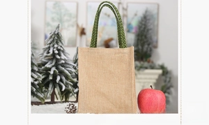 Side view of rustic burlap Christmas gift bag with green checkered handles and holiday decor