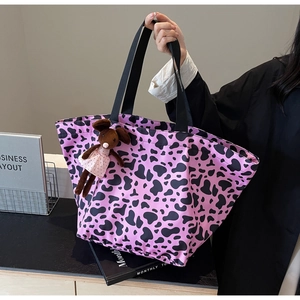 Pink and black cow print tote bag detail featuring a cute teddy bear charm hanging on handle