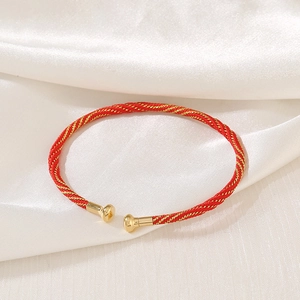 Close-up of red and gold woven rope bracelet with metallic round caps on white silk