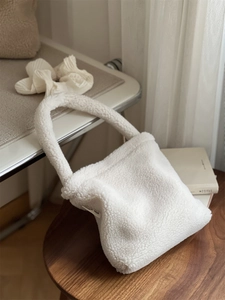 Detailed close-up of white plush sherpa handbag with simple wish label on a stool