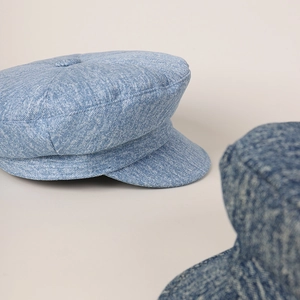Detail of light blue newsboy cap featuring denim texture and classic top button design