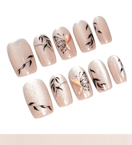 Détail d'ongles cat-eye champagne avec motifs de feuilles noires et de papillons délicats