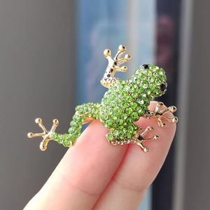 Close-up of a frog brooch with green rhinestones and golden metal frame held by hand