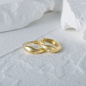 Macro detail of gold wave hoop earrings featuring star engravings and CZ stone inlay