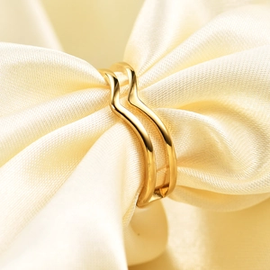 Macro detail of a 5mm double-layered golden V-shaped wave ring on silk fabric background