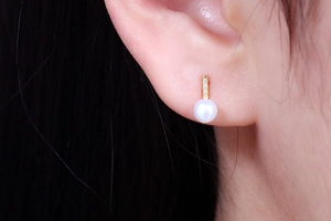 Macro shot of a long bar pearl stud earring with pavé diamonds on a golden metal bar