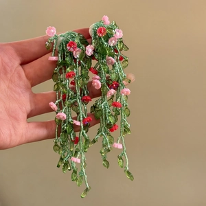 Detail of green beaded vine earrings with small pink and red flowers for a vacation look.