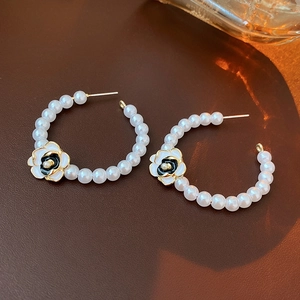 Close-up of C-shaped pearl hoop earrings with gold-plated metal and camellia flower detail
