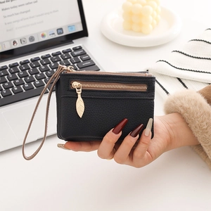 Detail view of black pebble leather wallet with golden leaf zipper and wrist strap