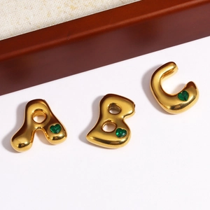 Pendentifs alphabet dorés A B C avec pierres de cœur vertes sur fond blanc épuré